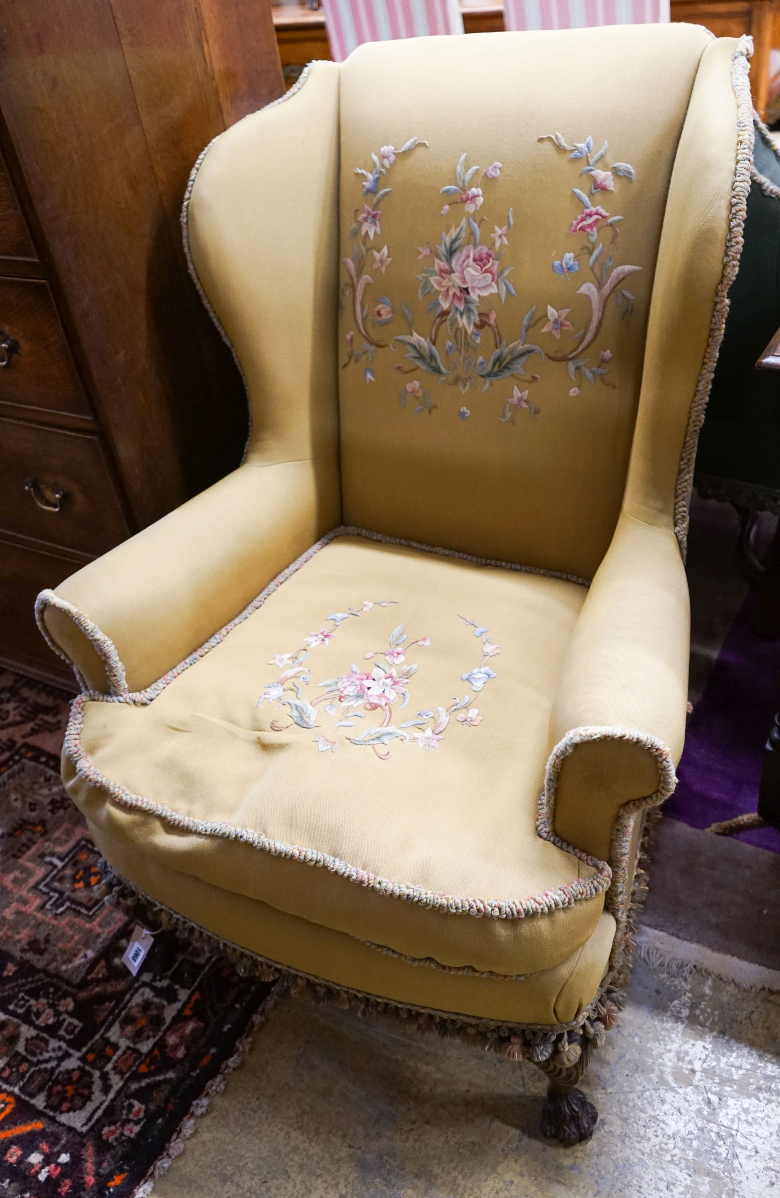 A wing frame armchair, upholstered in gold with embroidered flowers, on carved lion’s paw feet, width 80cm, depth 80cm, height 102cm